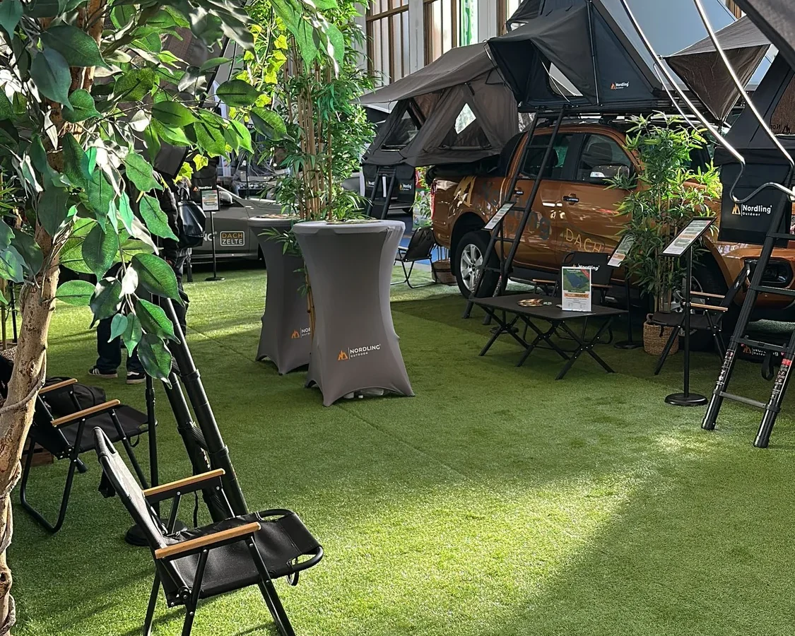 The Nordling Outdoor booth at a 2025 trade fair, rooftop tents set up on vehicles under the exhibition-hall lights.