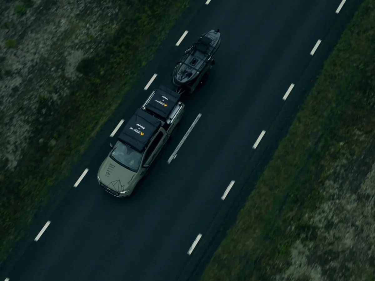 Aerial view straight down on the Green Beast pickup with rooftop tent and trailer driving a grey road between trees.