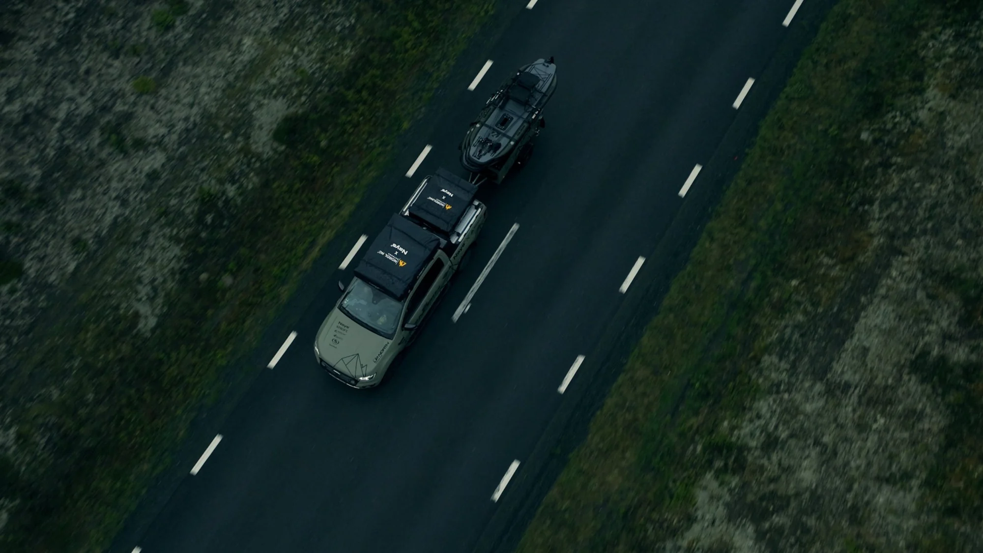 Aerial view straight down on the Green Beast pickup with rooftop tent and trailer driving a grey road between trees.