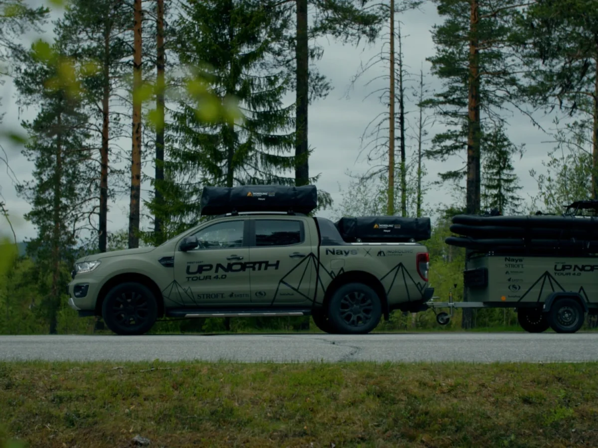 The Green Beast pickup and trailer in olive green with the UPNORTH livery, side on, parked at a forest edge.