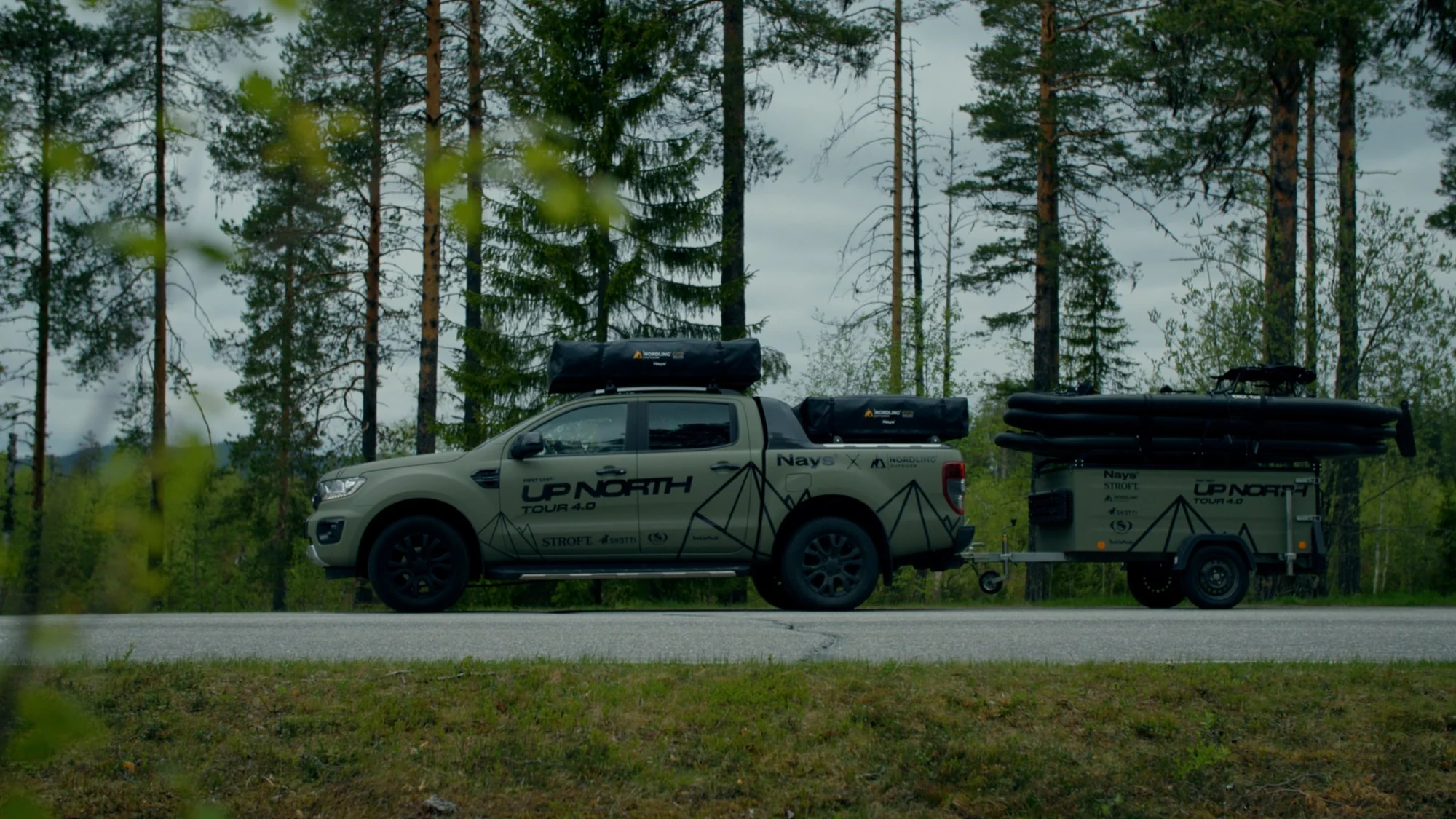 The Green Beast pickup and trailer in olive green with the UPNORTH livery, side on, parked at a forest edge.