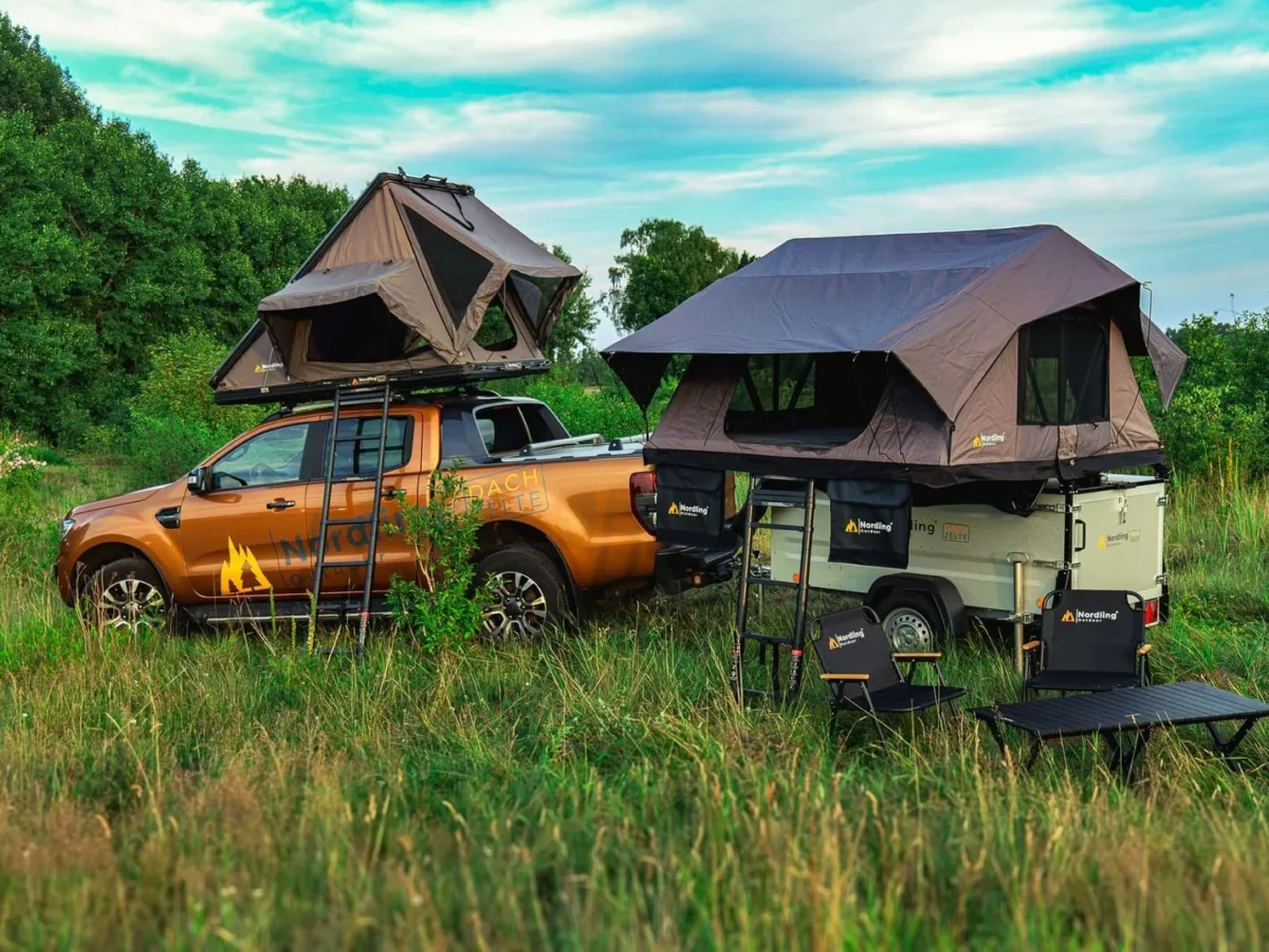 An orange pickup with a rooftop tent and a matching trailer with a second tent, parked in a green meadow: the vehicle before the UPNORTH livery.