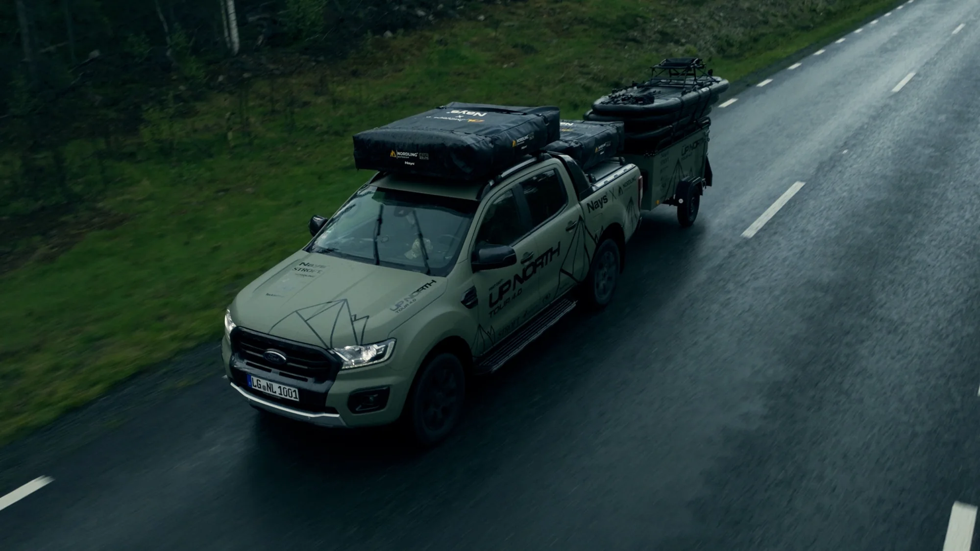 The Green Beast and its trailer on a wet country road between fields, seen from above.